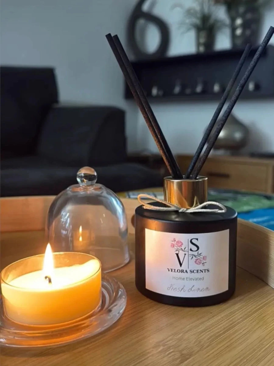 Velora Scents Fresh Linen luxury black bottle with gold collar and black sticks on wooden tray next to lit candle – home fragrance Cyprus